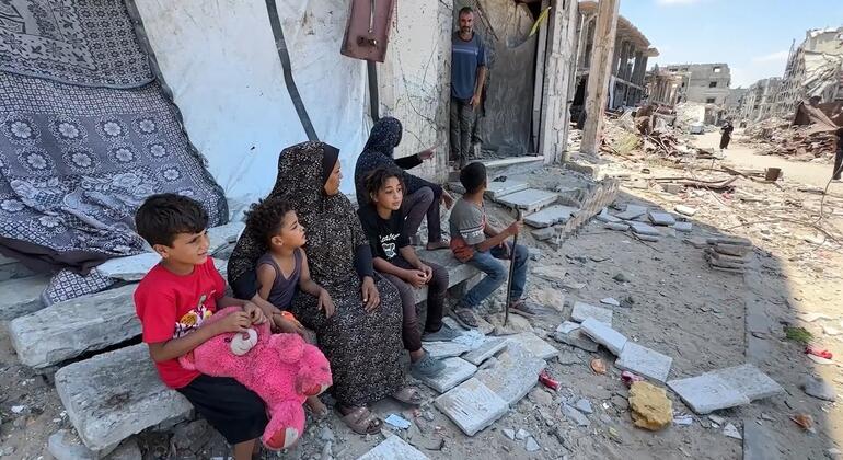 Una familia palestina desplazada permanece sentada sobre los escombros a las afueras de un edificio dañado en Gaza, en medio de la destrucción generalizada.